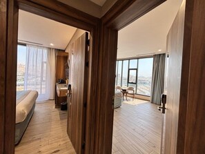 A hotel room with a bed, a desk with a chair, a small table, and a view of the city through large windows. - Nasamat Makkah Hotel (Makkah)
