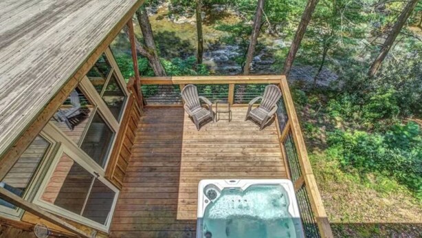 A wooden deck with a hot tub, two chairs, and a glass-enclosed room.