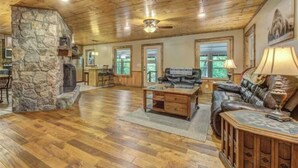 A spacious living area with a stone fireplace, wooden flooring, a leather sofa, and a dining area with a table and chairs.