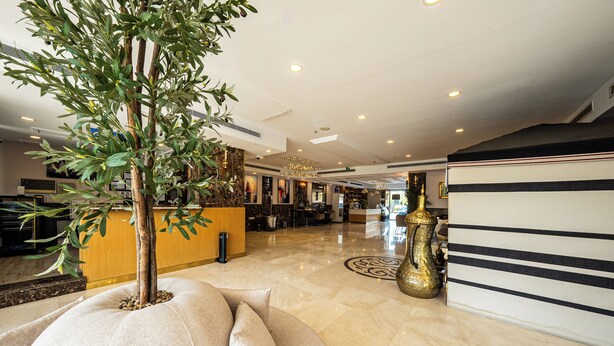 A hotel lobby with a reception desk, a large plant, a decorative vase, and a striped wall.