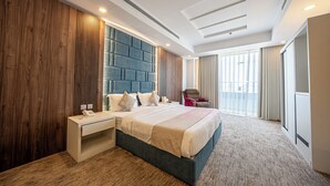 A modern hotel room with a large bed, a bedside table, a built-in headboard, and a large window with curtains.