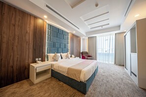 Una habitación de hotel moderna con una cama grande, una mesita de noche, cabecero integrado y un ventanal con cortinas.