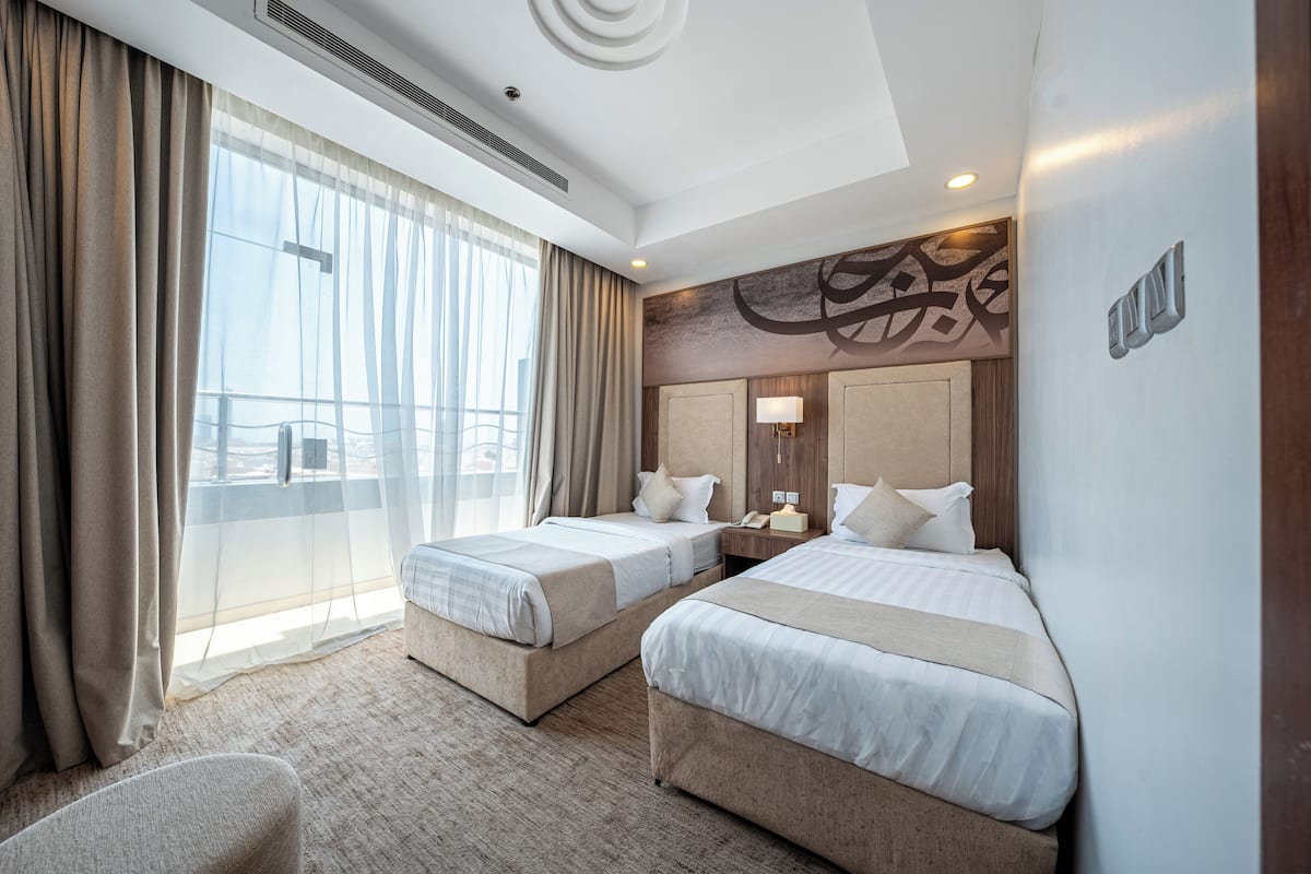 Une chambre d’hôtel avec deux lits, une grande fenêtre avec des rideaux, un climatiseur fixé au mur et un luminaire au plafond.