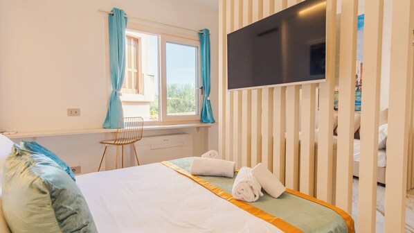 Une chambre d’hôtel avec un lit, un téléviseur fixé au mur, une fenêtre avec des rideaux et une chaise.