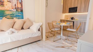 Ein modernes Hotelzimmer mit einem Bett, einer Essecke mit Tisch und Stühlen, einer Küchenzeile und einem großen Fenster mit Blick auf die Stadt.