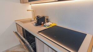 Eine Küche mit einem schwarzen Induktionskochfeld, einem goldenen Wasserhahn und einem Geschirrspüler.