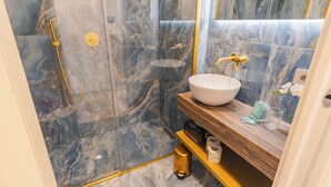Ein Badezimmer mit Marmorwand, Waschbecken in Weiß, goldenen Armaturen und einem Holzkosmetikschrank.