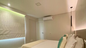 Un dormitorio moderno con una cama grande, una mesita de noche, aire acondicionado instalado en la pared y una ventana con persianas.