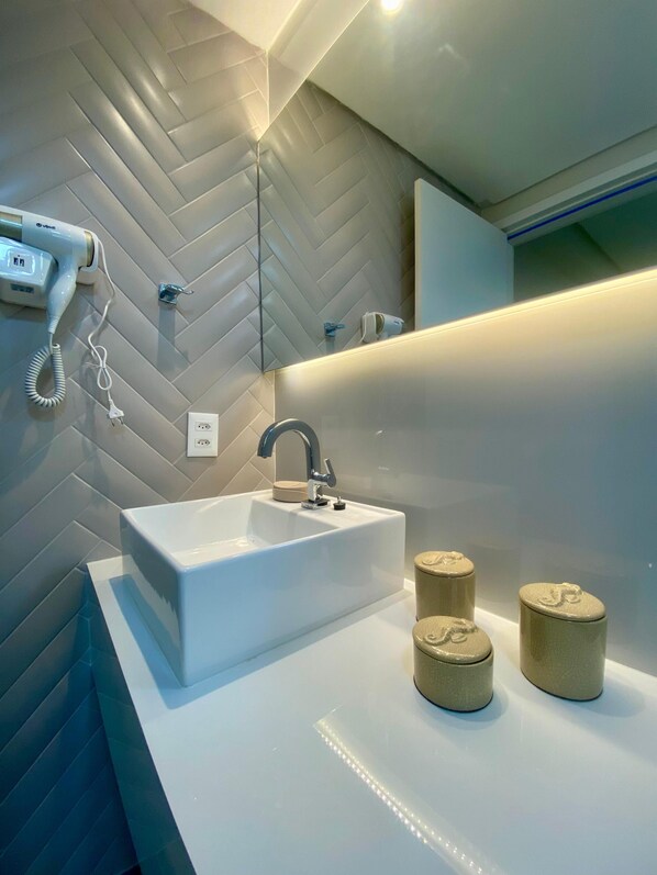 A modern bathroom with a white sink, a mirror, and a hairdryer mounted on the wall. - Casa 81 Luxo Pé na Areia Muro Alto byLP (Ipojuca)
