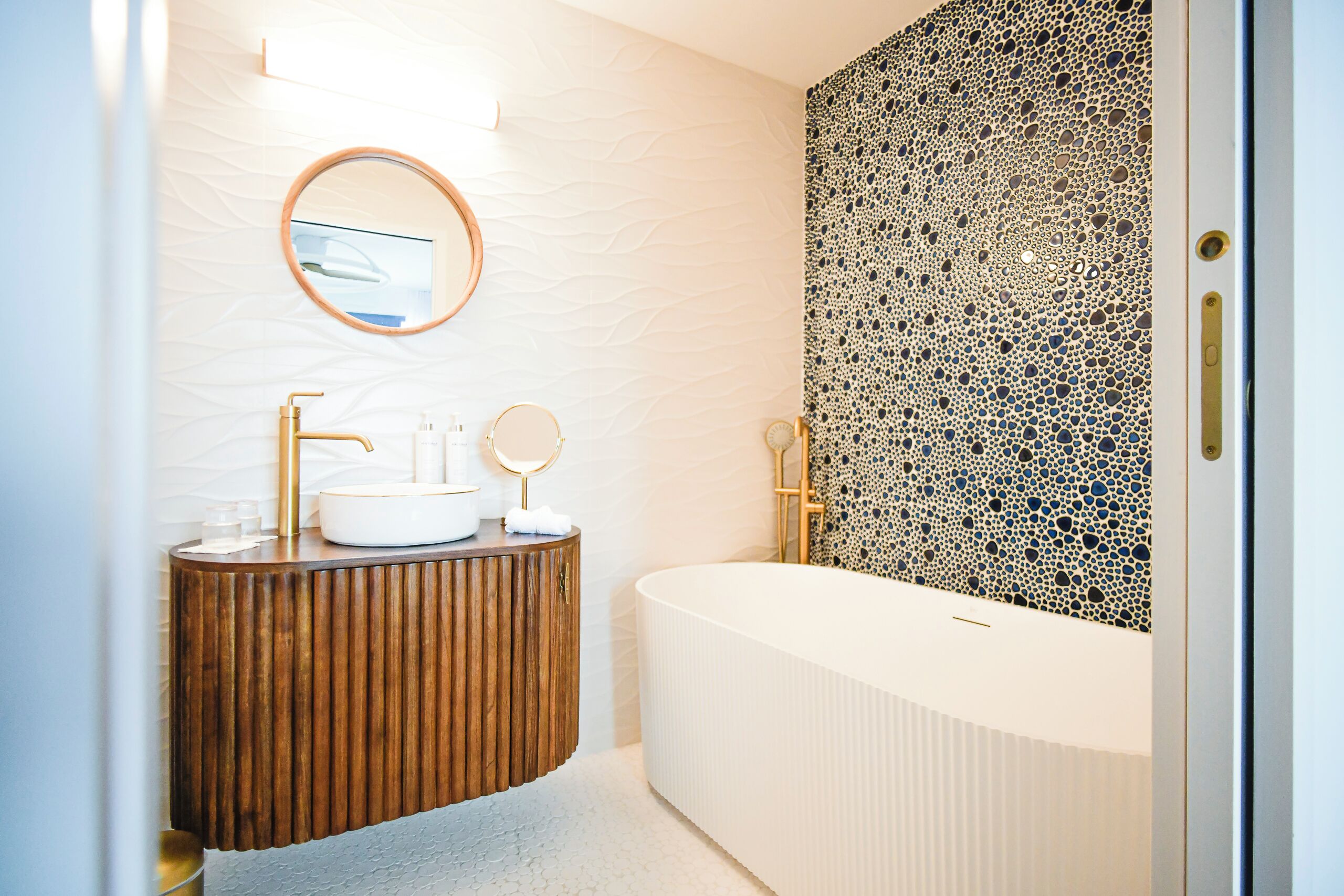 A modern bathroom with a wooden vanity, a round mirror, a white sink, and a freestanding bathtub.