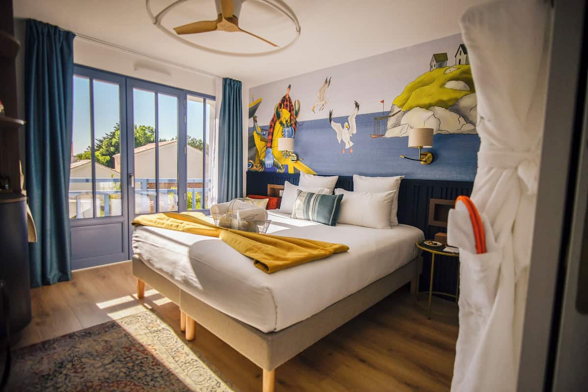 A hotel room with a large bed, a small bedside table, a ceiling fan, and a view of the outdoors.