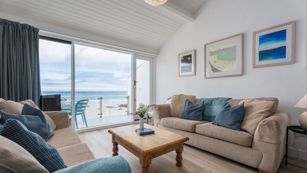 A living room with a beige sofa, a wooden coffee table, and a view of the beach through a sliding glass door.