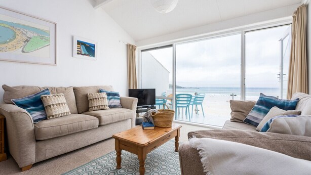 A living room with a sofa, a coffee table, and a TV. There is a large window with a view of the beach.