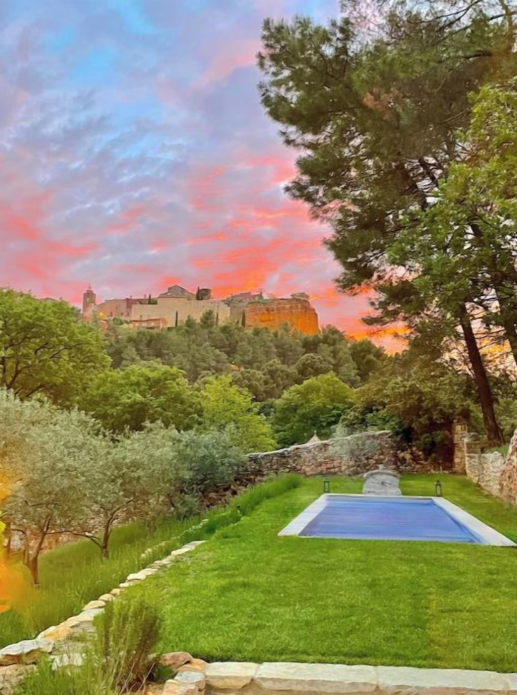 A pool with a stone border, surrounded by a well-maintained lawn and trees.