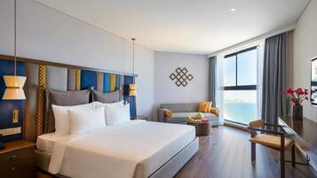 A hotel room with a large bed, a sofa, a small table, and a view of the sea.