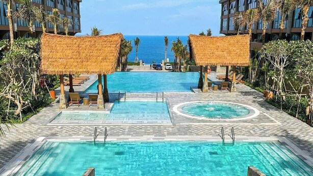 A resort pool with a slide, palm trees, and a view of the ocean.