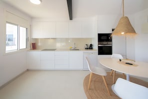 A modern kitchen with white cabinets, a dining table with chairs, a hanging light fixture, and a view of the outside.