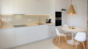 A modern kitchen with white cabinets, a round dining table, and a hanging light fixture.
