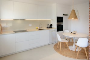A modern kitchen with white cabinets, a round dining table, and a hanging light fixture.