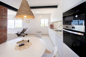 A modern kitchen with a large oven, a hanging light fixture, and a dining area with a table and chairs.