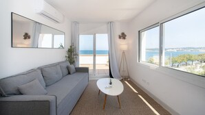 A modern room with a grey sofa, a small white table, and a large window offering a view of the sea.