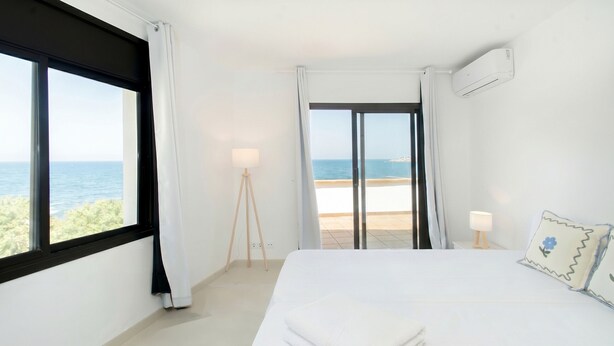 A hotel room with a bed, a lamp, a view of the sea, and an air conditioning unit.