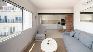 A modern living room with a grey sofa, a small white table, a grey armchair, and a kitchen in the background.