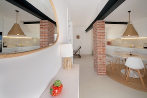 A modern kitchen with a round dining table, white chairs, and a hanging light fixture.