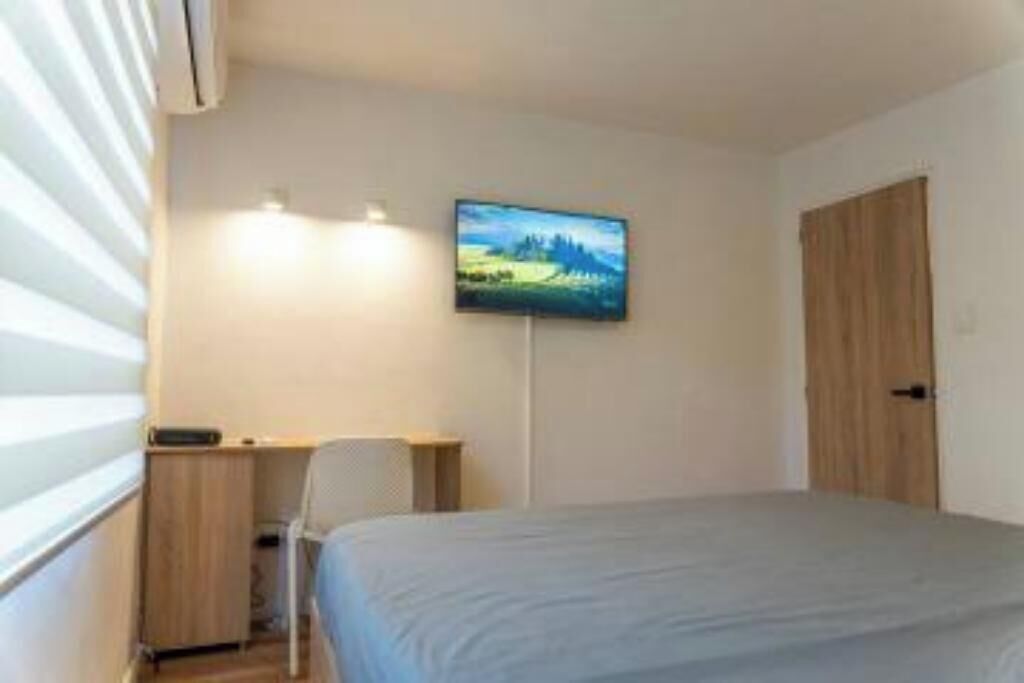 Ein Schlafzimmer mit einem Bett, einem Schreibtisch, einem Stuhl, einem an der Wand befestigten Fernseher und einer Tür.