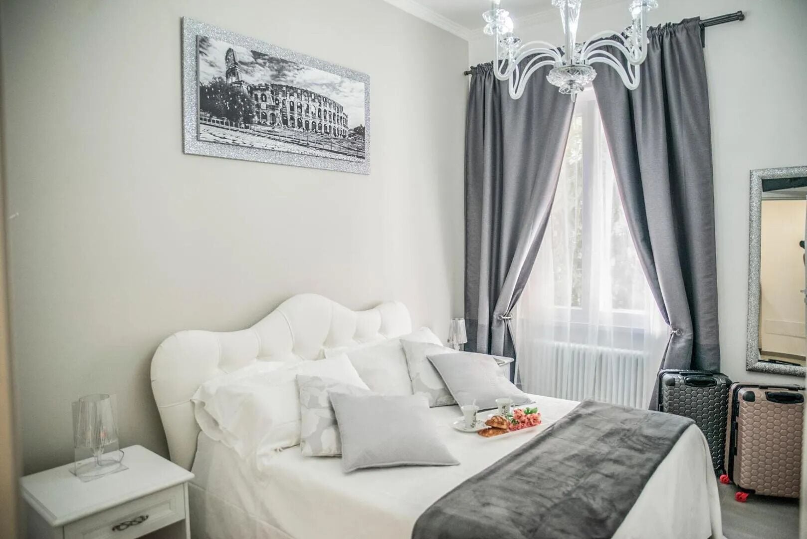 Un lit bien fait, avec des oreillers et une couverture, une table de chevet avec un verre, un tableau représentant un bâtiment accroché au mur et une fenêtre avec des rideaux.