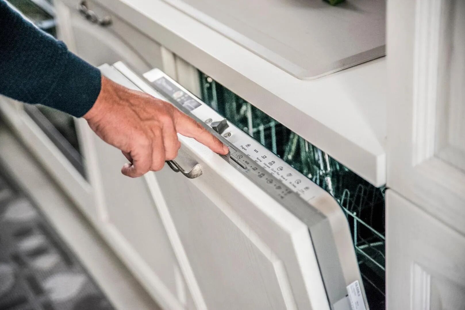 Una persona che utilizza un pannello di controllo su un elettrodomestico bianco, probabilmente una lavastoviglie, dotato di display digitale e vari pulsanti.
