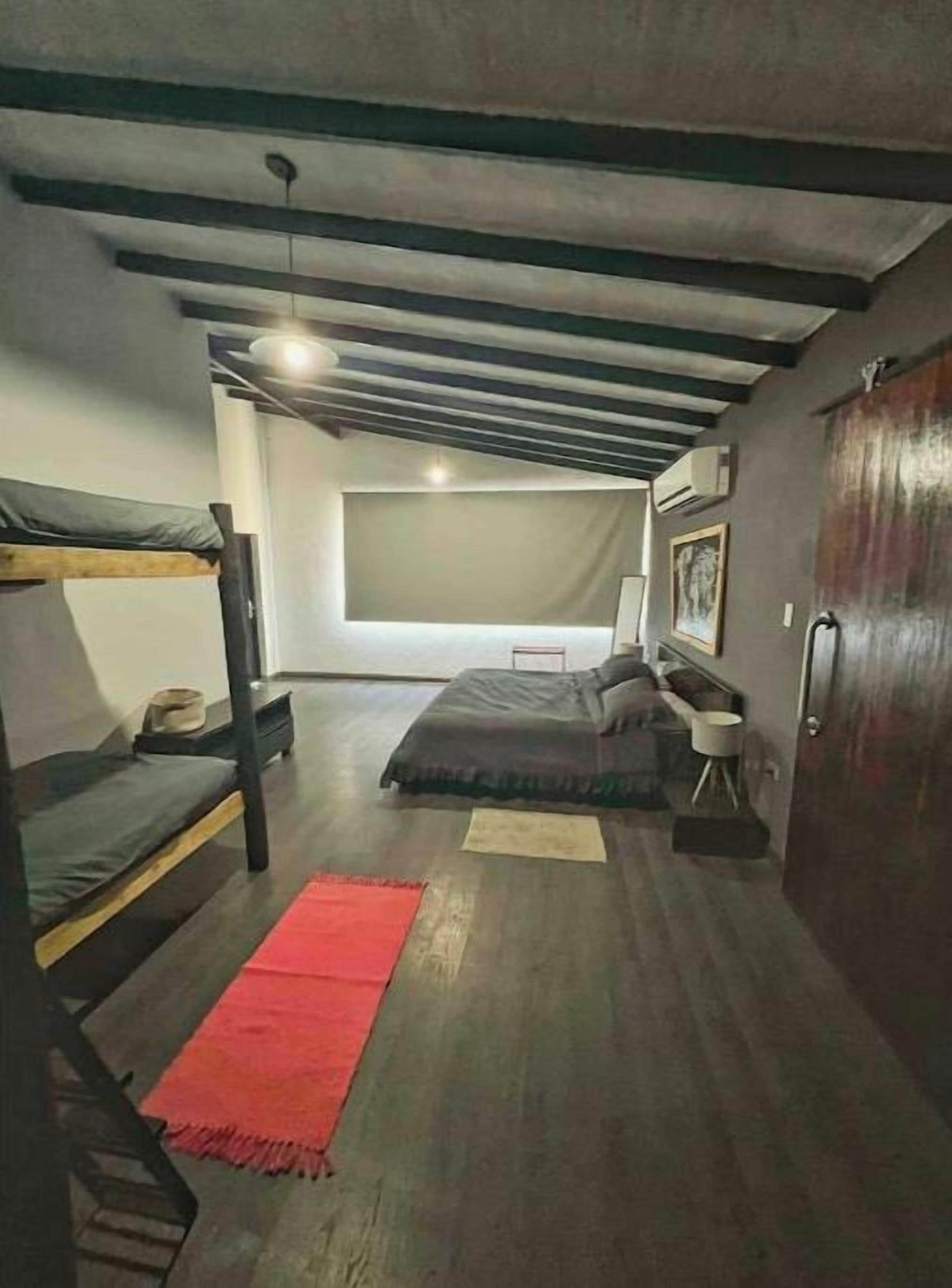 Een slaapzaal met stapelbedden, een rood vloerkleed, een klein tafeltje en een raam met uitzicht.