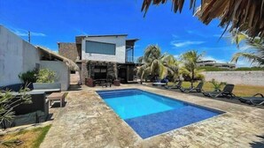 Una casa moderna con piscina, mobiliario exterior y palmeras.