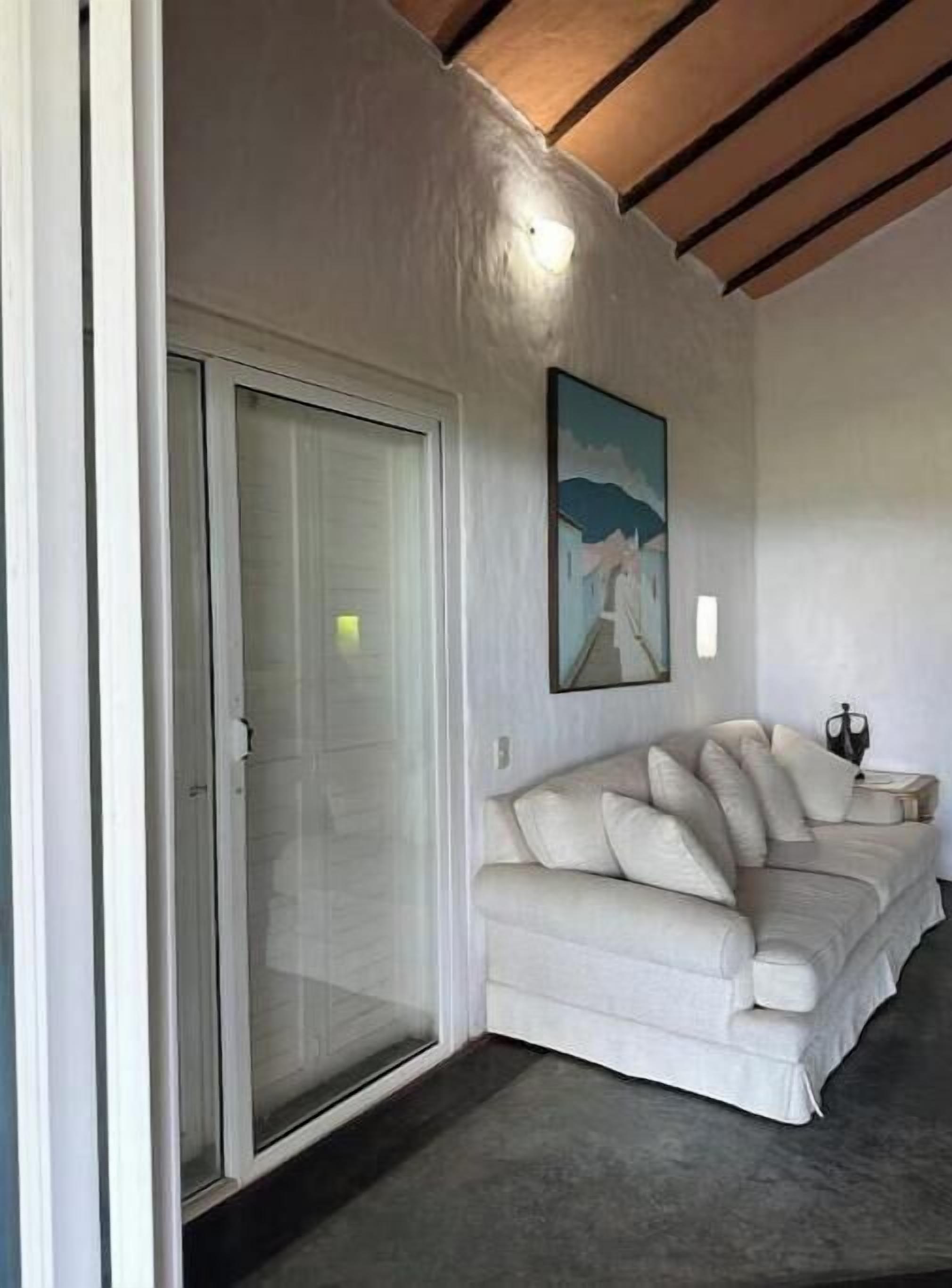 Un salon moderne avec un canapé blanc, une porte en verre et un tableau accroché au mur.