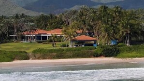 A beachfront property with a house and a covered area, surrounded by palm trees and a beach.
