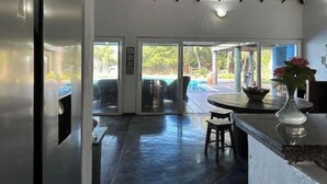 A modern kitchen with a dark floor, a bar area with stools, and a view of an outdoor pool area through glass doors.