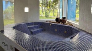 A hot tub with a checkered blue tile pattern, two decorative vases, and a view of palm trees through large windows.