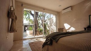 A bedroom with a large bed, a view through a sliding glass door to an outdoor area, and a hanging rope. - Colonial House Pool + parking (Mérida)