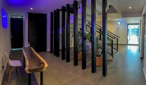 A modern interior with a long wooden table and chairs, a staircase, and potted plants.