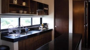 A modern kitchen with dark wood cabinets, a black countertop, and a built-in oven. There are hanging lights above the counter and a window providing natural light. - Comfortable and modern Loft-Exclusive Area Merida (Mérida)