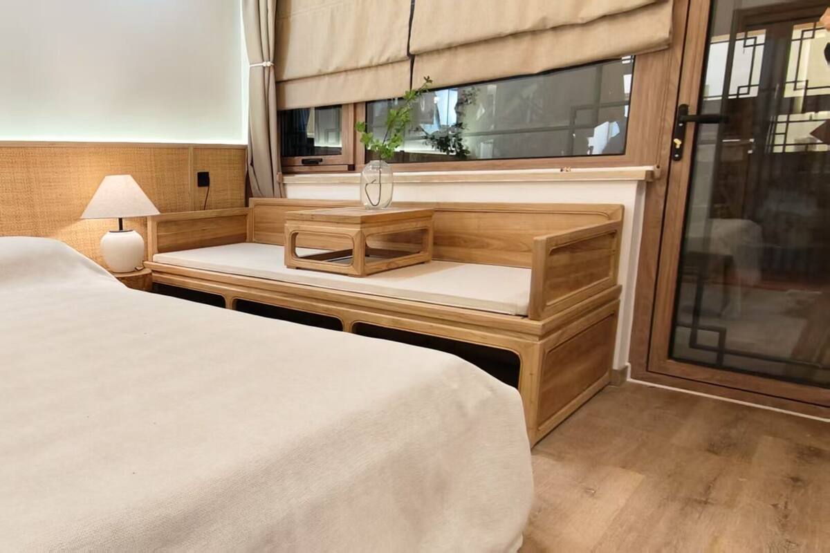 A hotel room with a large bed, a bedside table with a lamp, and a window with curtains.