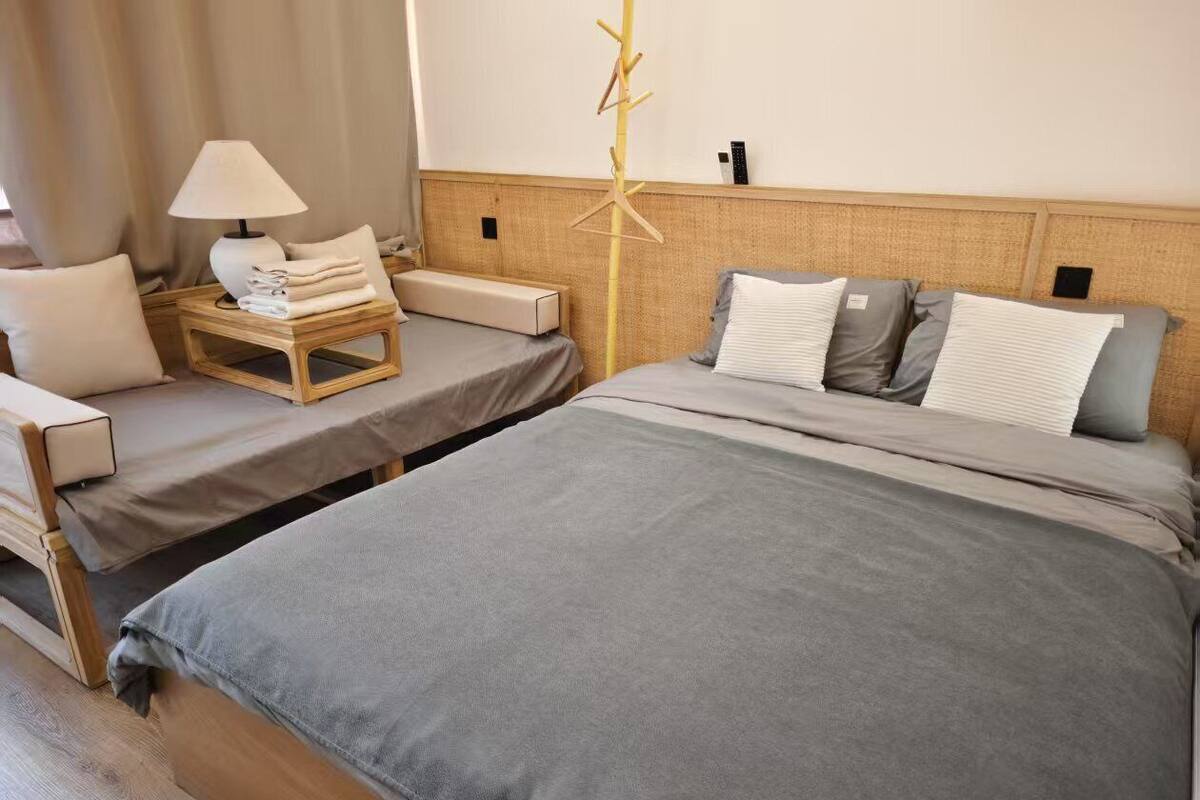 A hotel room with two beds, a bedside table with a lamp, a coat rack, and a bedside shelf.