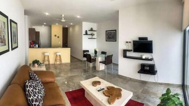A modern living room with a sofa, coffee table, and a dining area with chairs and a table.