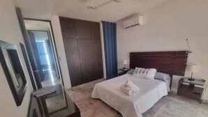A hotel room with a bed, a desk, a mirror, a wardrobe, and a ceiling fan.