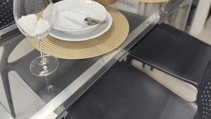A modern dining table with a clear glass top, white plates, and a woven placemat.