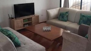 Uma sala de estar com sofá, mesa de centro e televisão sobre um armário de madeira.