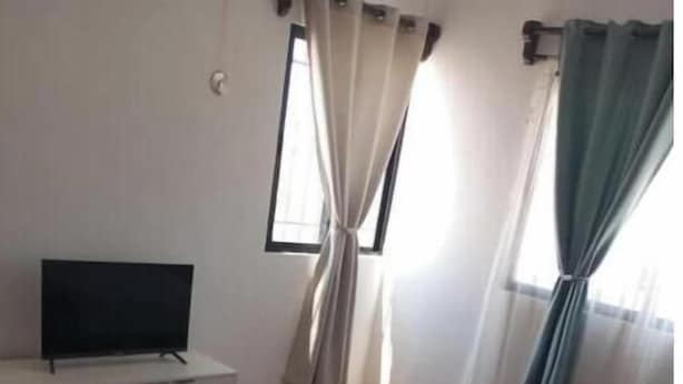 Quarto com duas camas, uma televisão sobre um móvel, janela com cortinas e piso de azulejos.