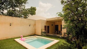 A rectangular swimming pool with a pink flamingo float in a backyard with artificial grass, surrounded by a low wall and trees. - Casa La María: luxury, comfort and private pool (Mérida)