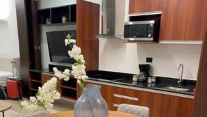 A modern kitchen with wooden cabinets, a microwave, and a sink. There is a dining table with four chairs and a vase with white flowers. - Urban Refuge, Loft with pool and cowork (Mérida)