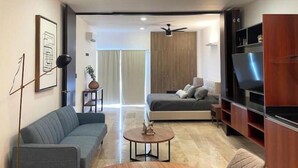 A modern living room with a sofa, a coffee table, a TV, and a bed with a ceiling fan. - Urban Refuge, Loft with pool and cowork (Mérida)